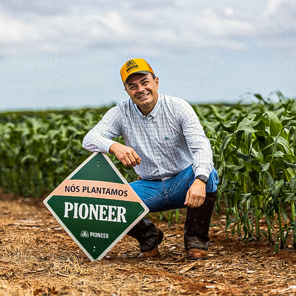 Homem agachado apoiando o braço numa placa Pioneer na lavoura
