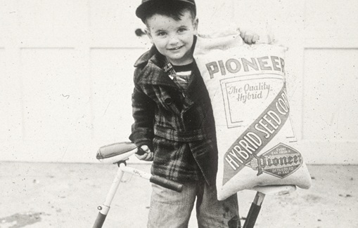 Legacy black and white photo - boy on bicycle holding Pioneer seed corn bag