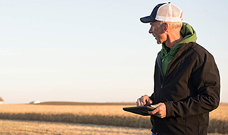 Man holding tablet beside partly harvested cornfield